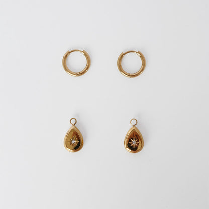 A pair of gold huggie hoop earrings and a pair of gold teardrop pendant earrings with a small star detail, arranged symmetrically on a light gray background.