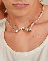 Person wearing a silver necklace with a neutral background