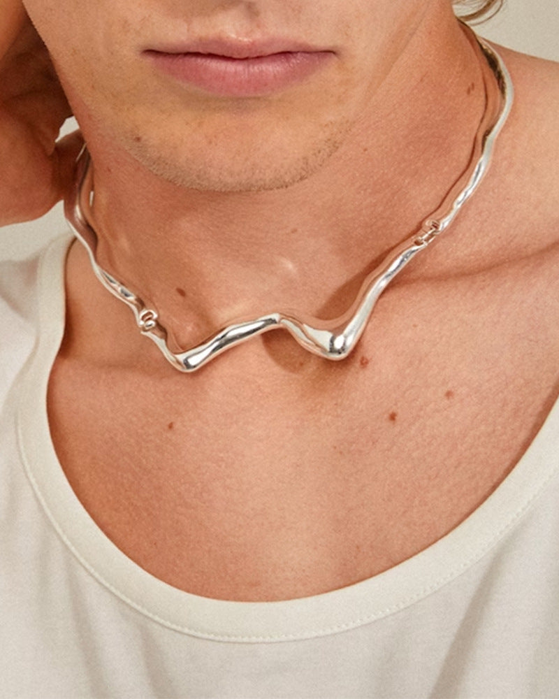 Person wearing a silver necklace with a neutral background