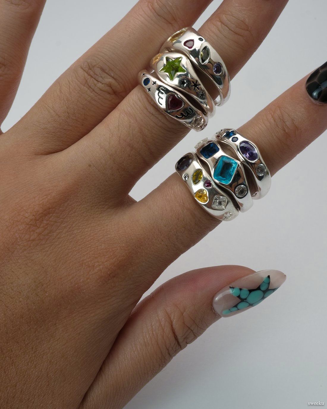 Stacked silver rings with multi-colored gems, worn on hand