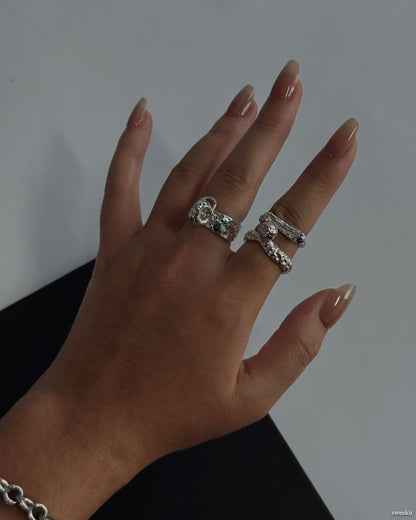 Hand wearing the Sculpted Orbit Trio Ring Set with three sculptural silver bands stacked together.