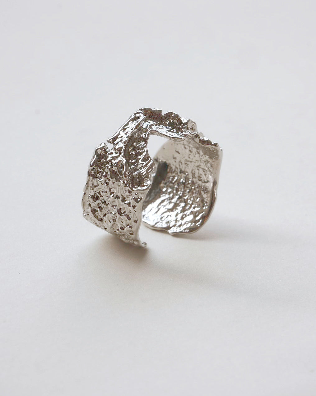 Side view of abstract textured sculptural ring with a wide, fluid design and adjustable band
