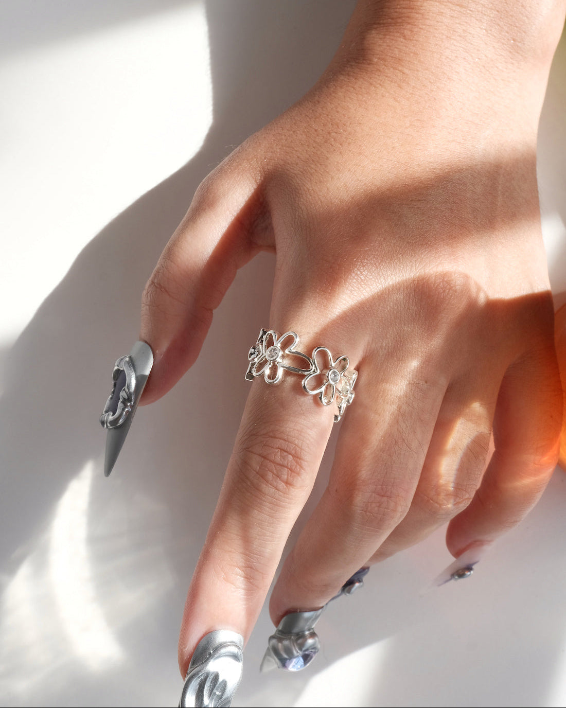Wearing down view of dainty flower adjustable ring with an open band and clear crystal accents
