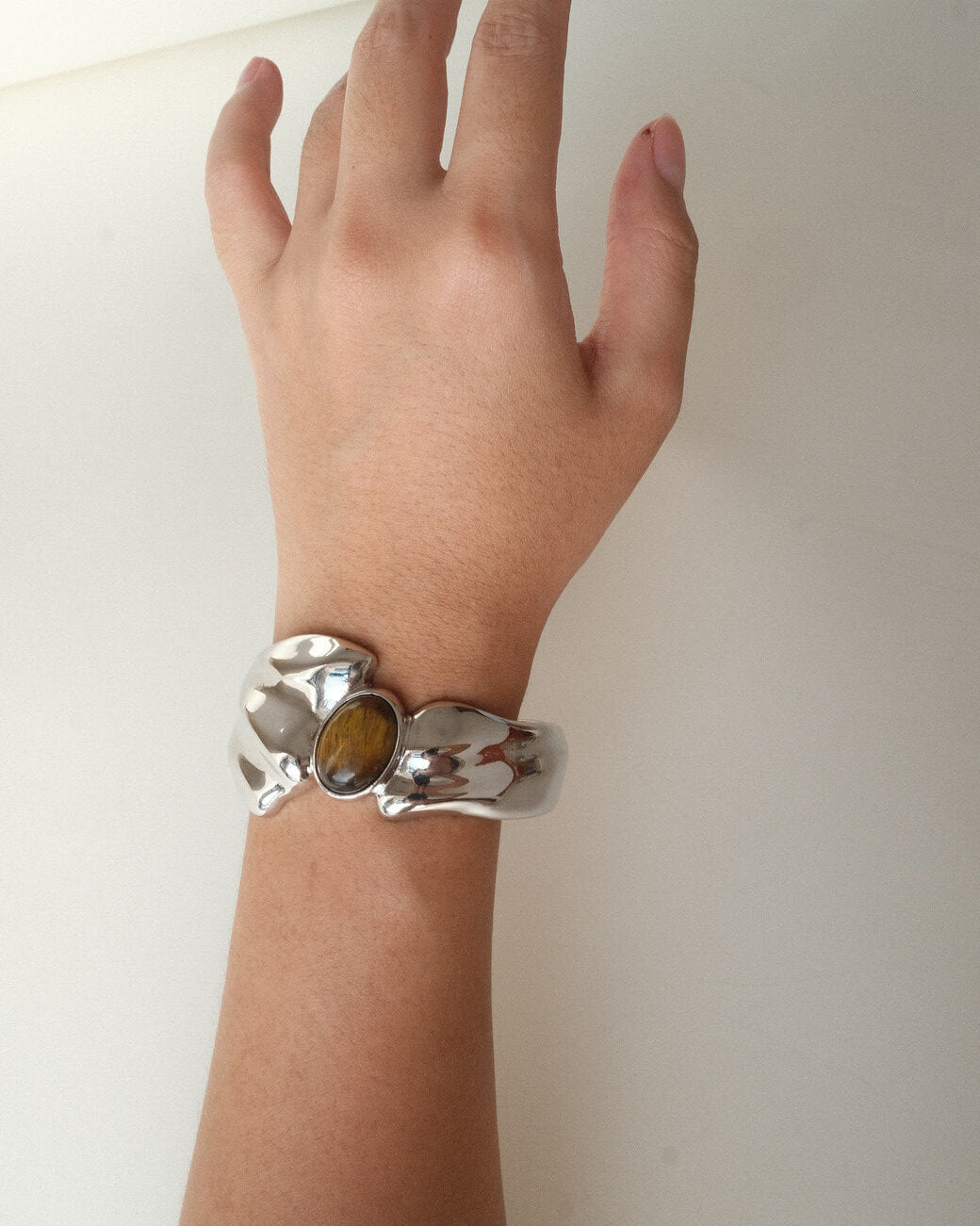 Model wearing sculptural liquid metal cuff bracelet with a polished finish and a central Tiger's Eye gemstone – hands up view – SWEEKU jewelry