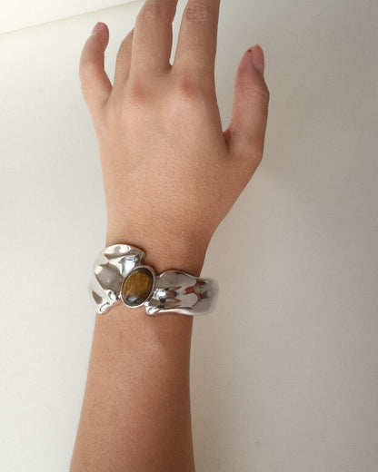 Model wearing sculptural liquid metal cuff bracelet with a polished finish and a central Tiger's Eye gemstone – hands up view – SWEEKU jewelry