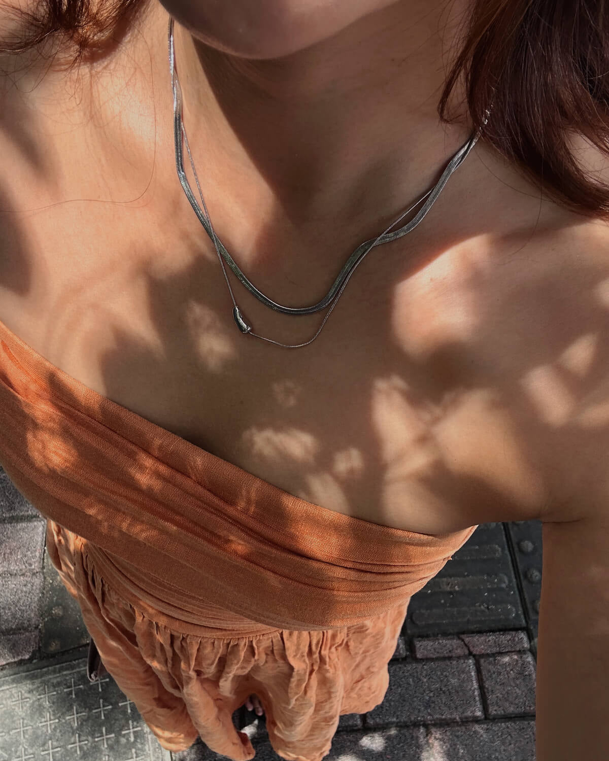 Model wearing two-layer snake chain necklace with a small, polished tear drop pendant - top view - SWEEKU jewelry