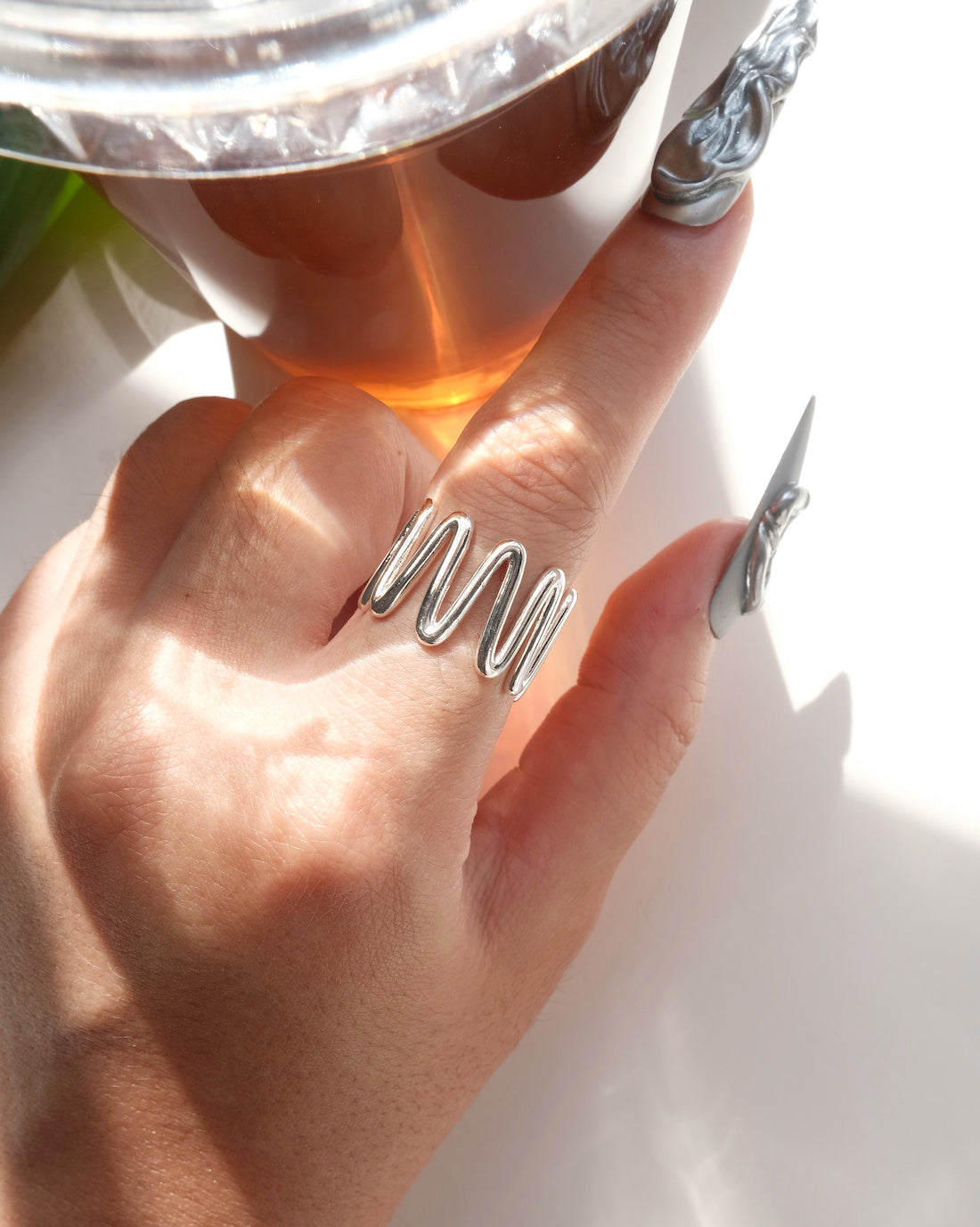 Top view of wearing of sculptural wavy line ring with a polished, fluid design and adjustable band
