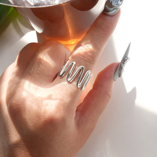 Top view of wearing of sculptural wavy line ring with a polished, fluid design and adjustable band
